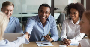 Team members smiling during a collaborative sales meeting, with a handshake signaling partnership or deal success.